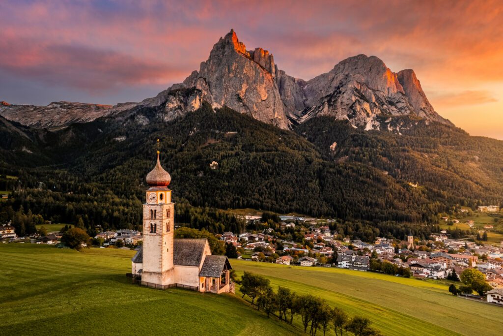 Seis am Schlern, Italien - Schöner Sonnenuntergang und luftige Berglandschaft in den italienischen Dolomiten mit St. Valentinskirche und dem berühmten Schlernberg mit bunten Wolken und warmem Sonnenlicht in Südtirol.