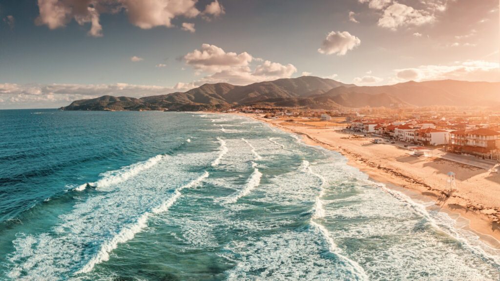 Dramatischer Panorama-Luftbildblick auf den ikonischen Ort Sarti und den berühmten langen, leeren Sandstrand im Sonnenuntergang bei hohen Wellen. Urlaub auf Halkidiki, Griechenland