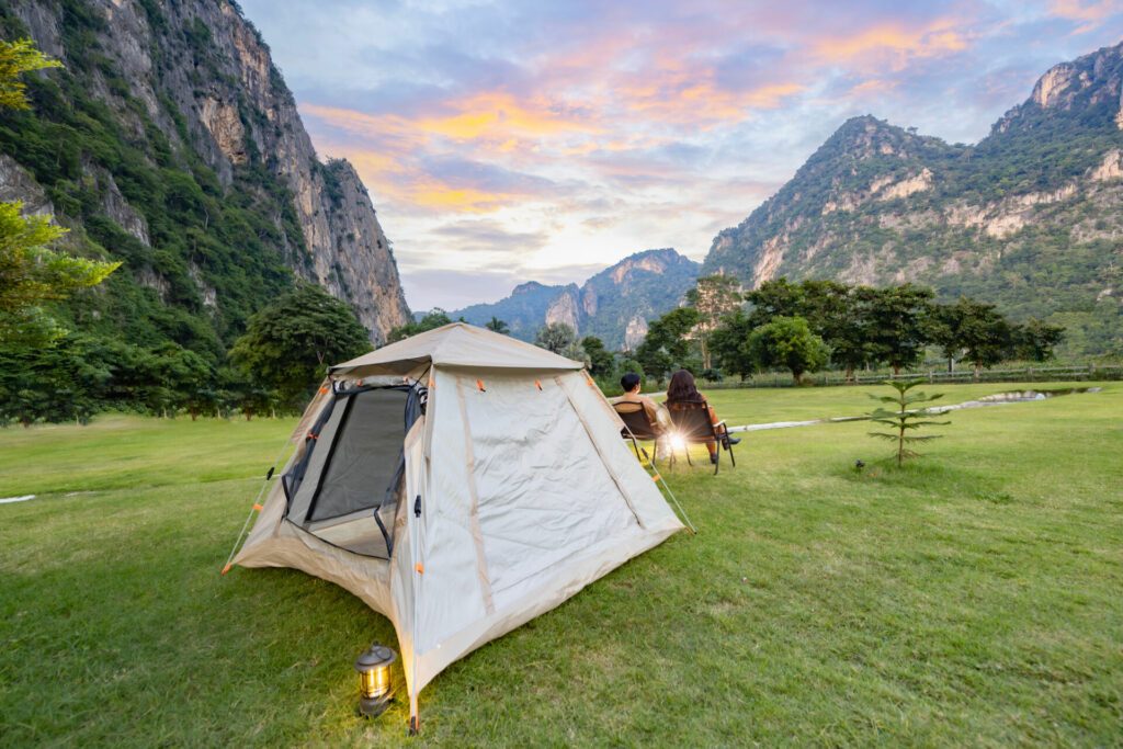 Camping und Zelt in der Natur. Abenteuerlicher Lifestyle von Mann und Frau, die in Campingstühlen sitzen und den schönen Sonnenuntergang über der Bergkette und die Aussicht auf die Natur genießen.